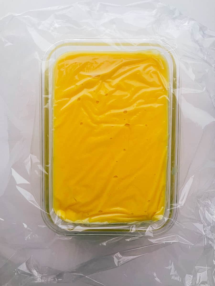 Finished passion fruit curd in a container with plastic wrap on top.