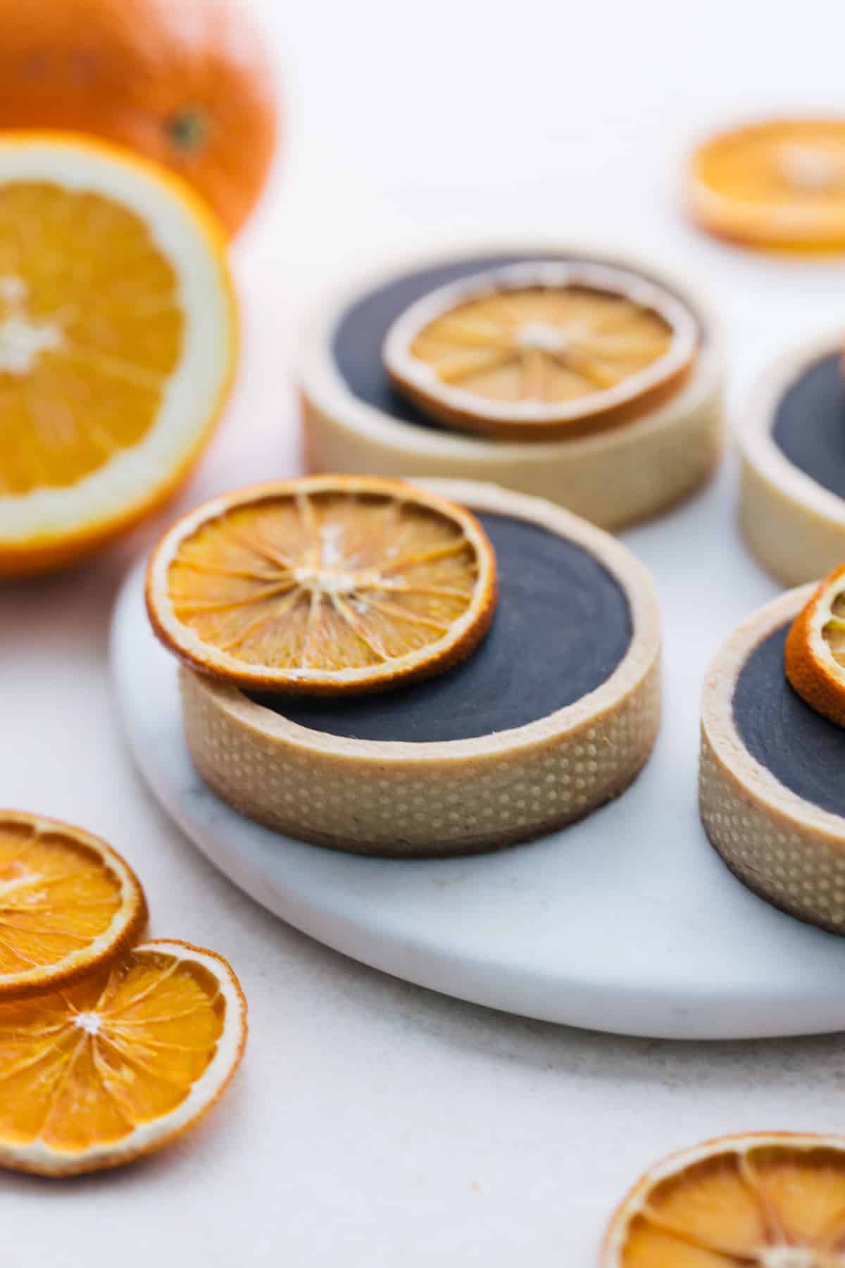 Orange Chocolate Ganache Tartlets on a marble plate with a dried orange on top.