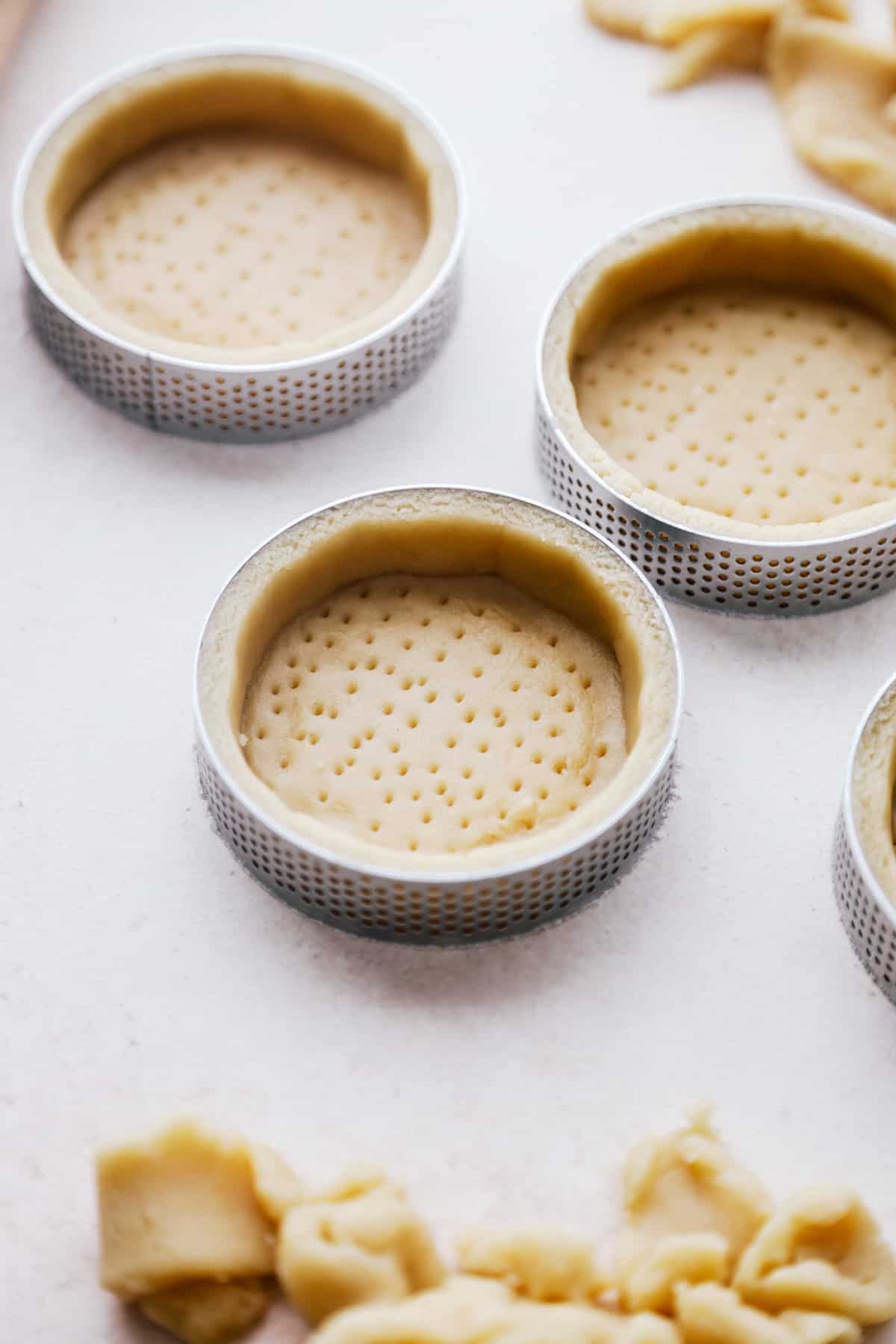Tart dough in mini perforated tart rings.