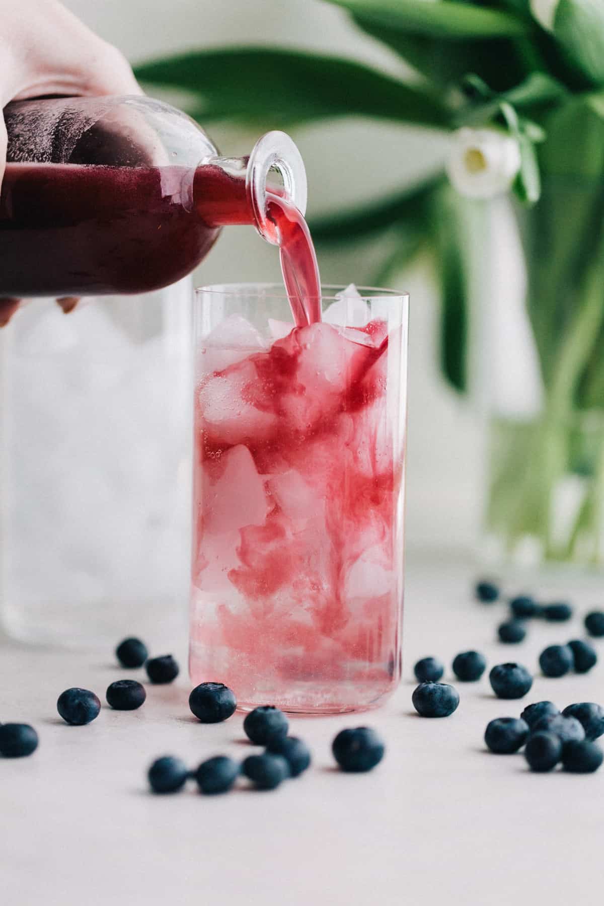 Pouring blueberry shrub over ice.