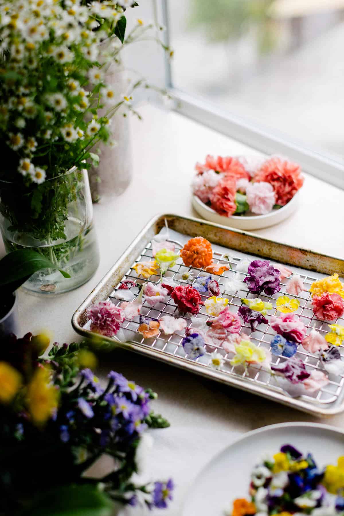 Sugared flowers on a cooling rack surrounded by fresh flowers.