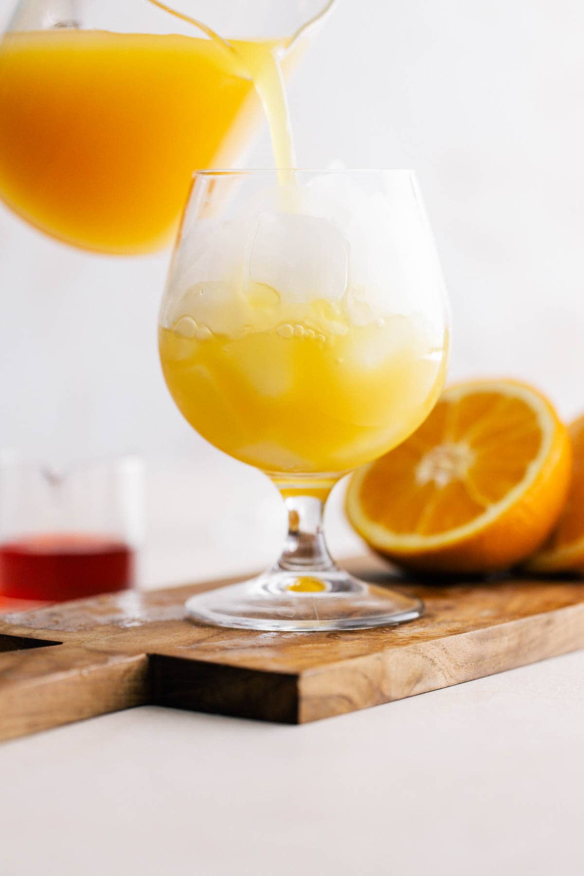 Adding orange juice and vodka into a cocktail glass with ice.