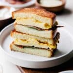 Brioche break breakfast sandwich with egg, avocado, and cheese on a plate.