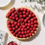 Whole chocolate raspberry tart on the counter with one slice cut.