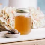 Jar of honey syrup on the counter with a bowl of honey.