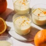 Four cups of orange posset with grate orange zest on top.