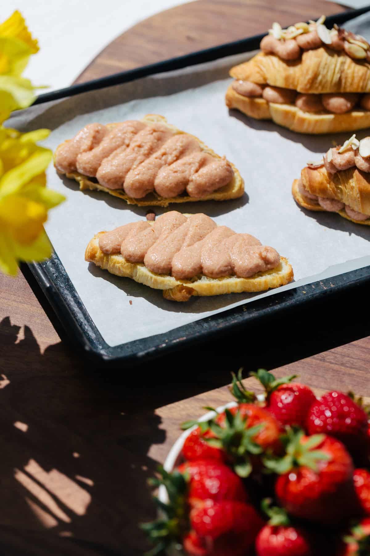 Piping strawberry frangipane onto croissants on a baking sheet. 