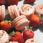 Strawberry macarons on the counter near fresh strawberries.