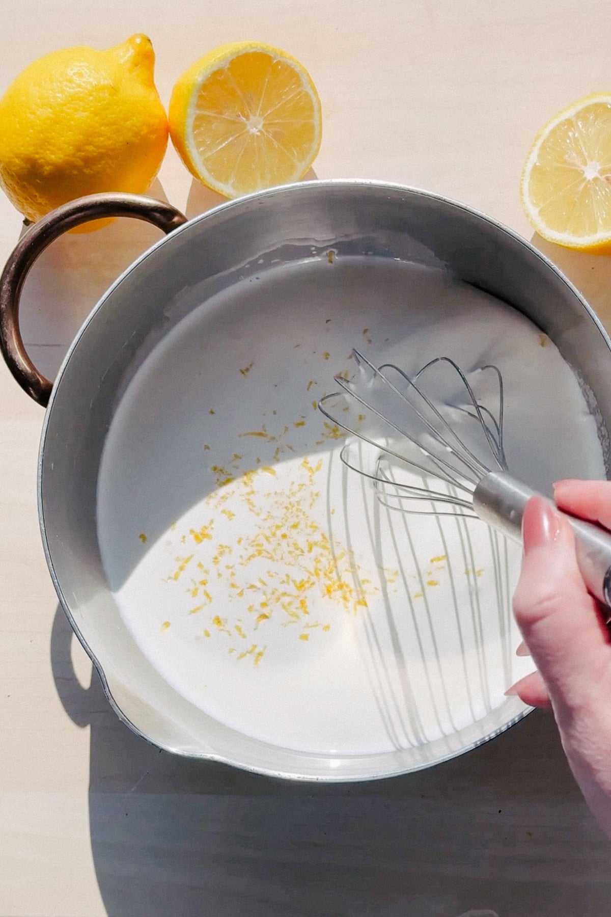 Infusing cream and sugar with lemon zest in a saucepan.