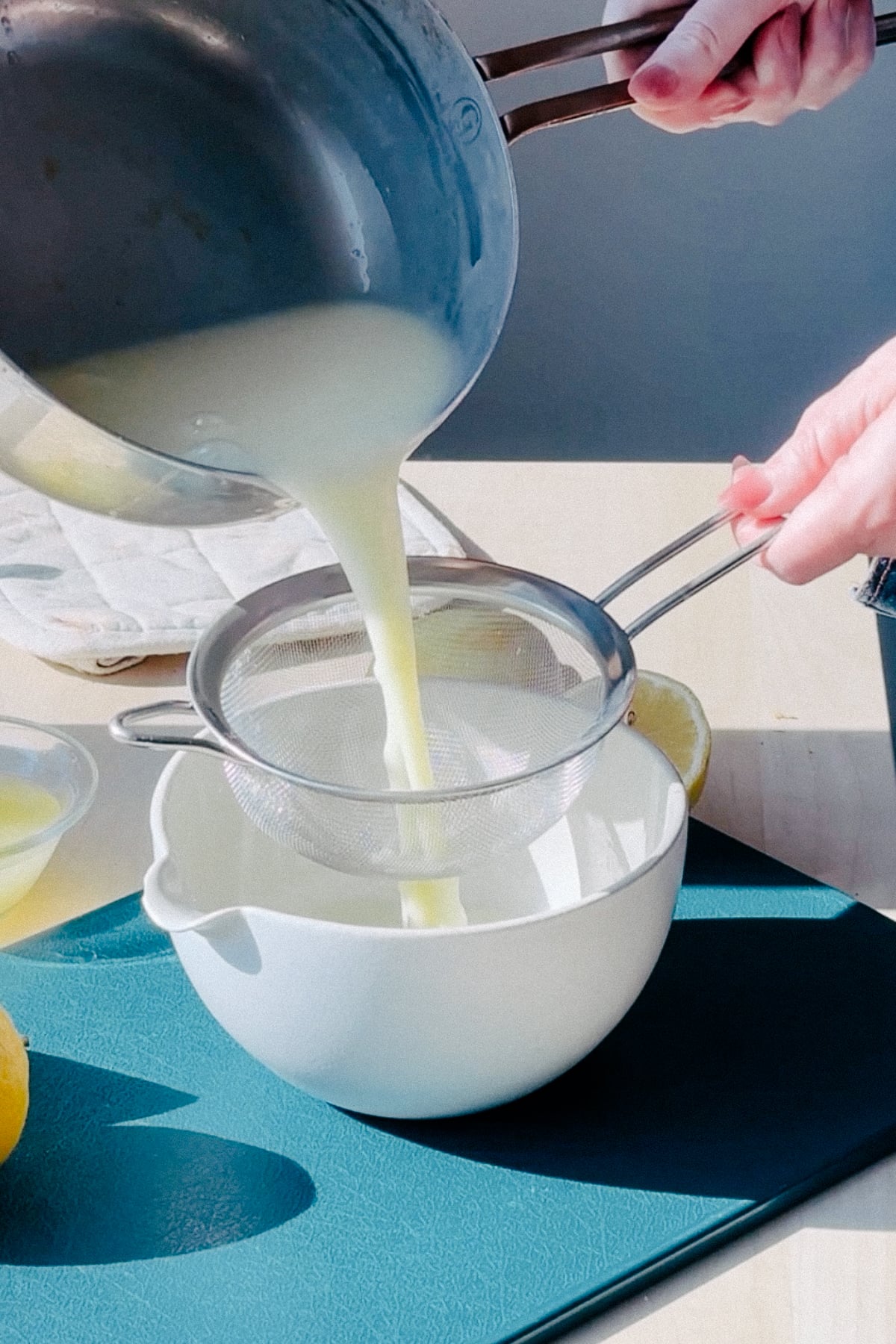 Straining posset base into a bowl with a fine mesh sieve.