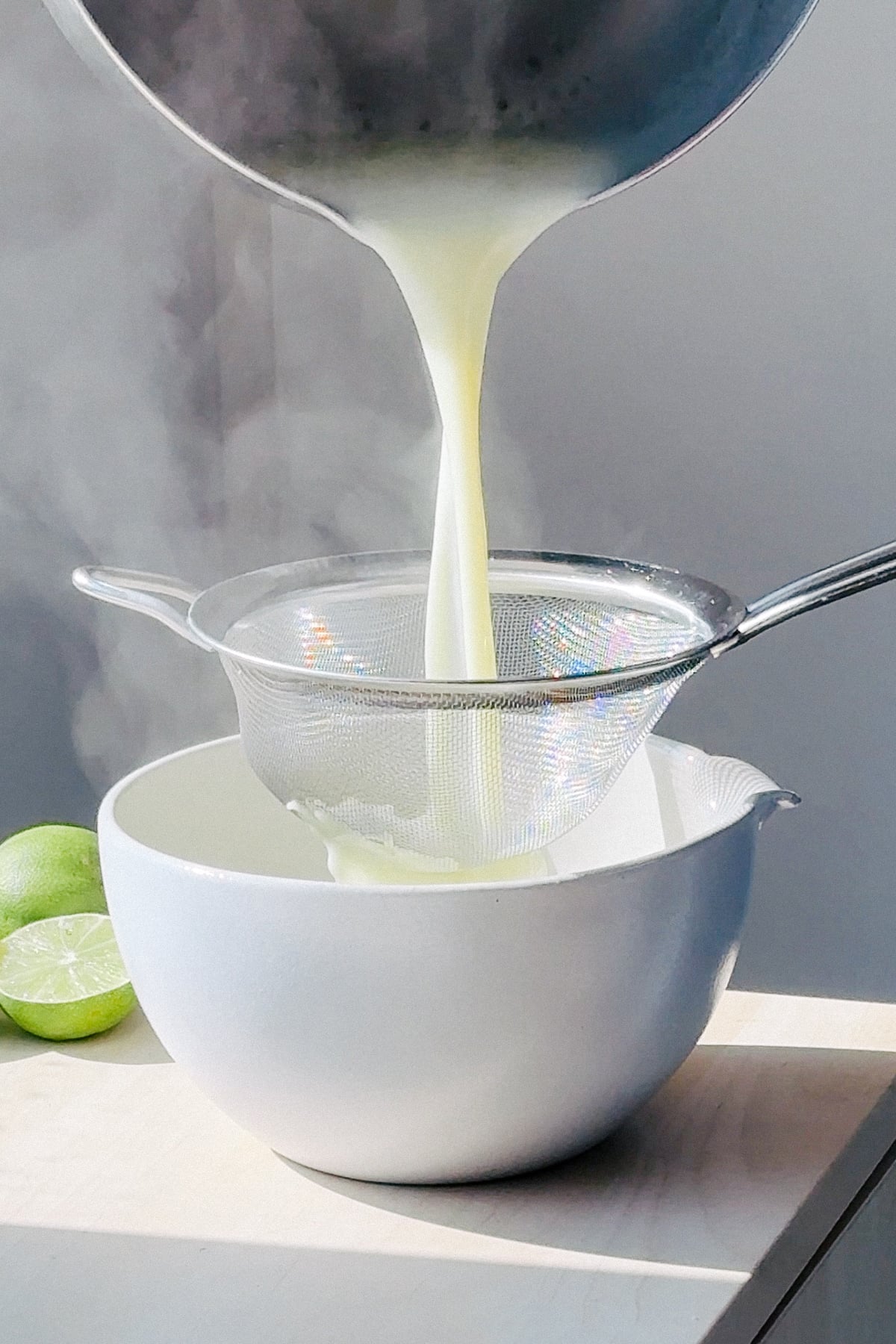 Straining posset base into a bowl with a fine mesh sieve.