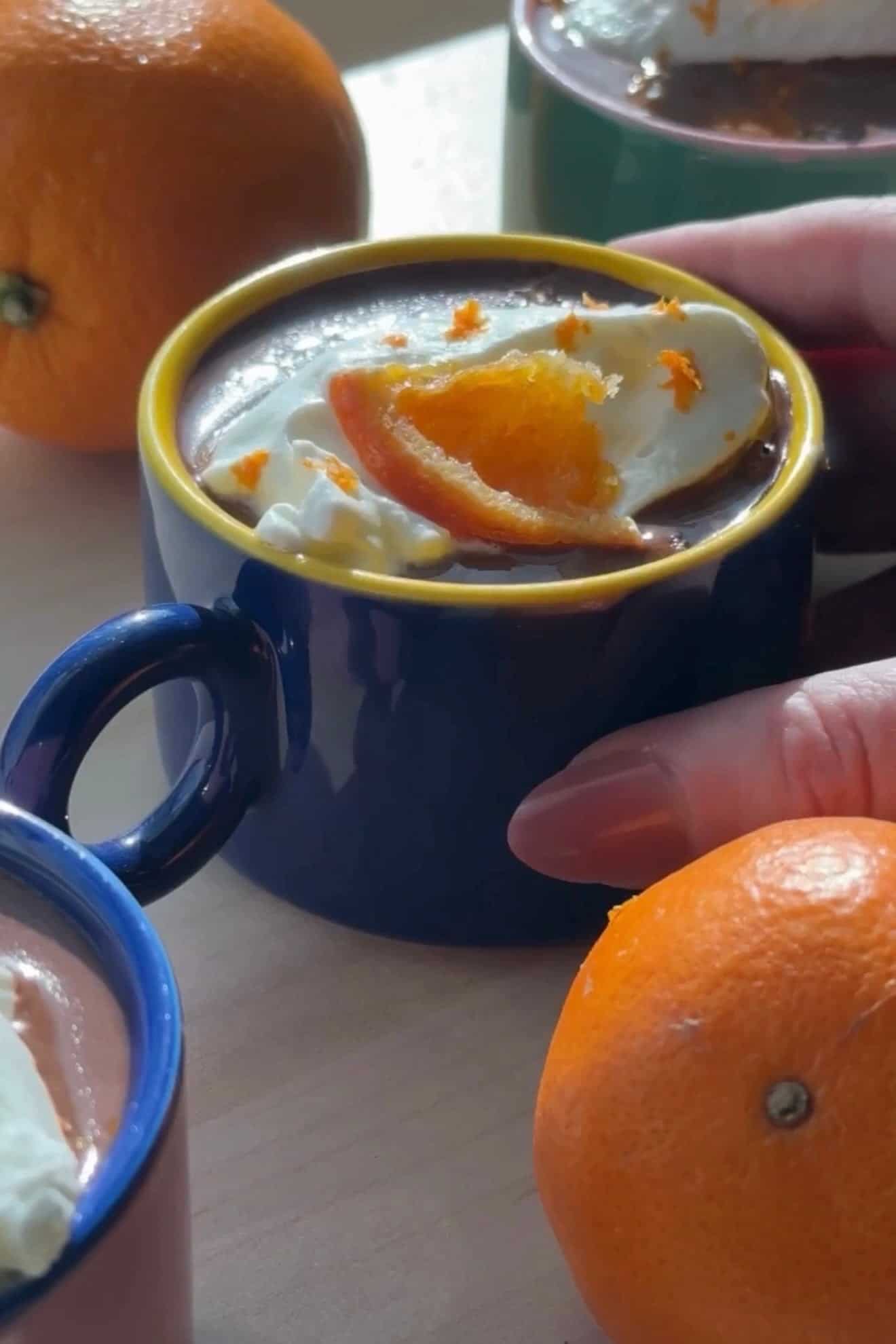 French hot chocolate with softly whipped cream and a candied orange in a blue mug