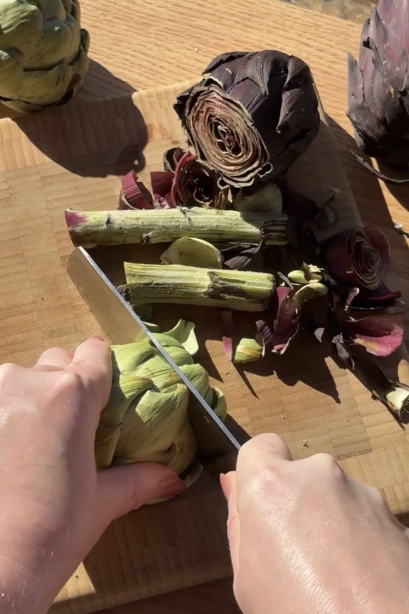 Trimming and prepping artichokes on a cutting board.