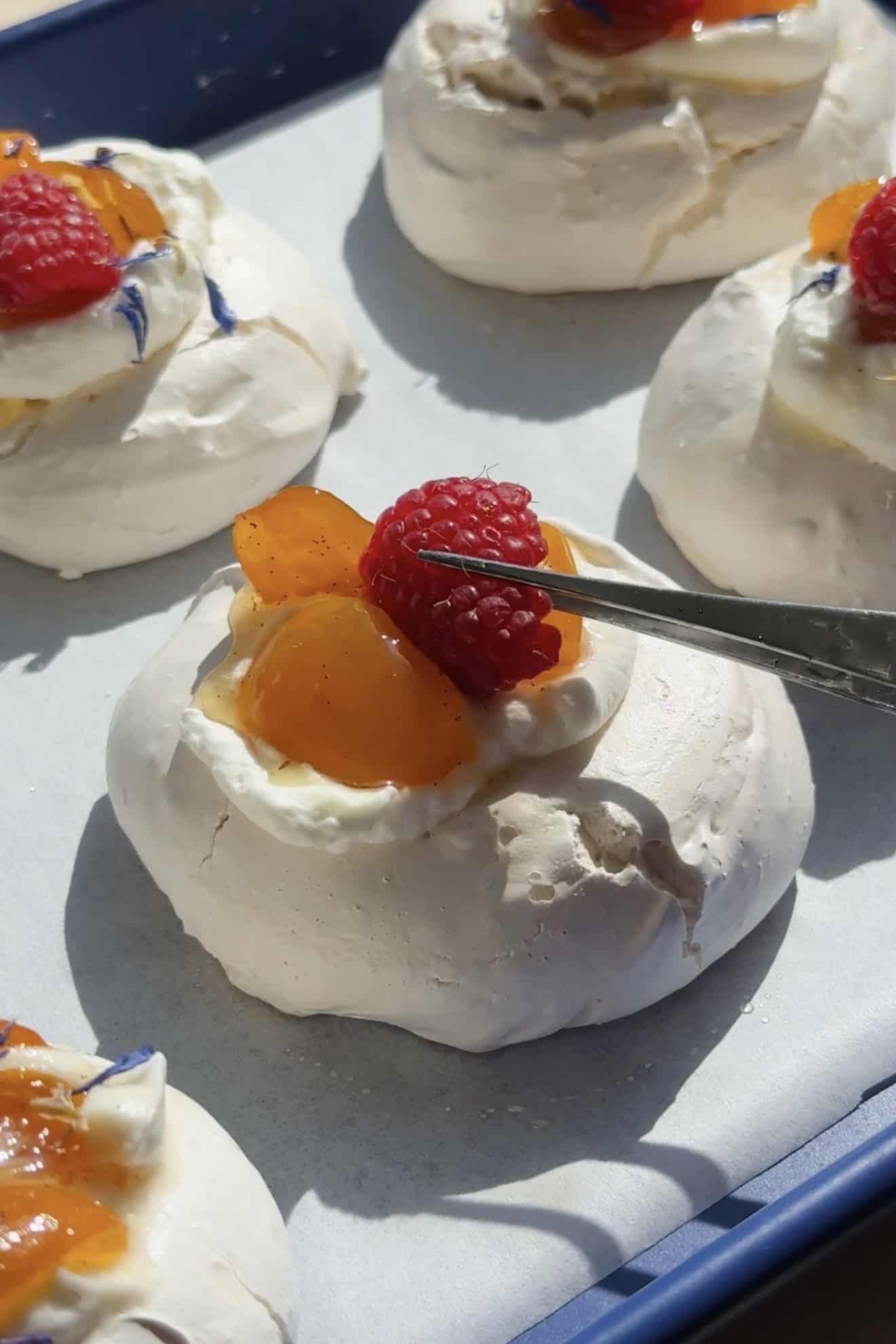 Adding kumquats and raspberries to the mini pavlovas.