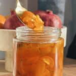 Candied kumquats in a glass jar with a spoon.