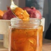 Candied kumquats in a glass jar with a spoon.