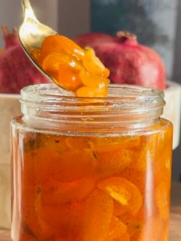 Candied kumquats in a glass jar with a spoon.