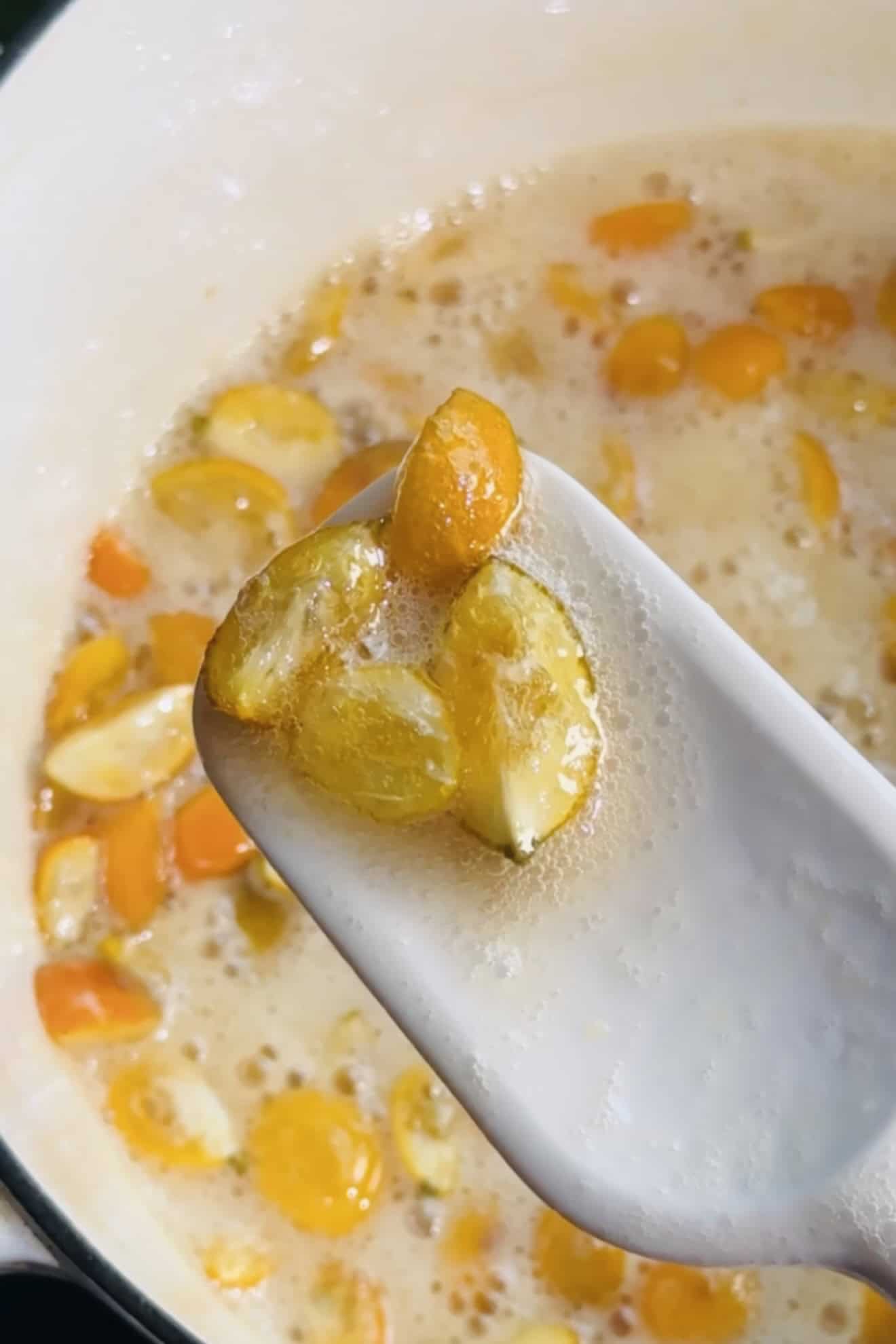 Candied kumquats on a spatula above the pot. 