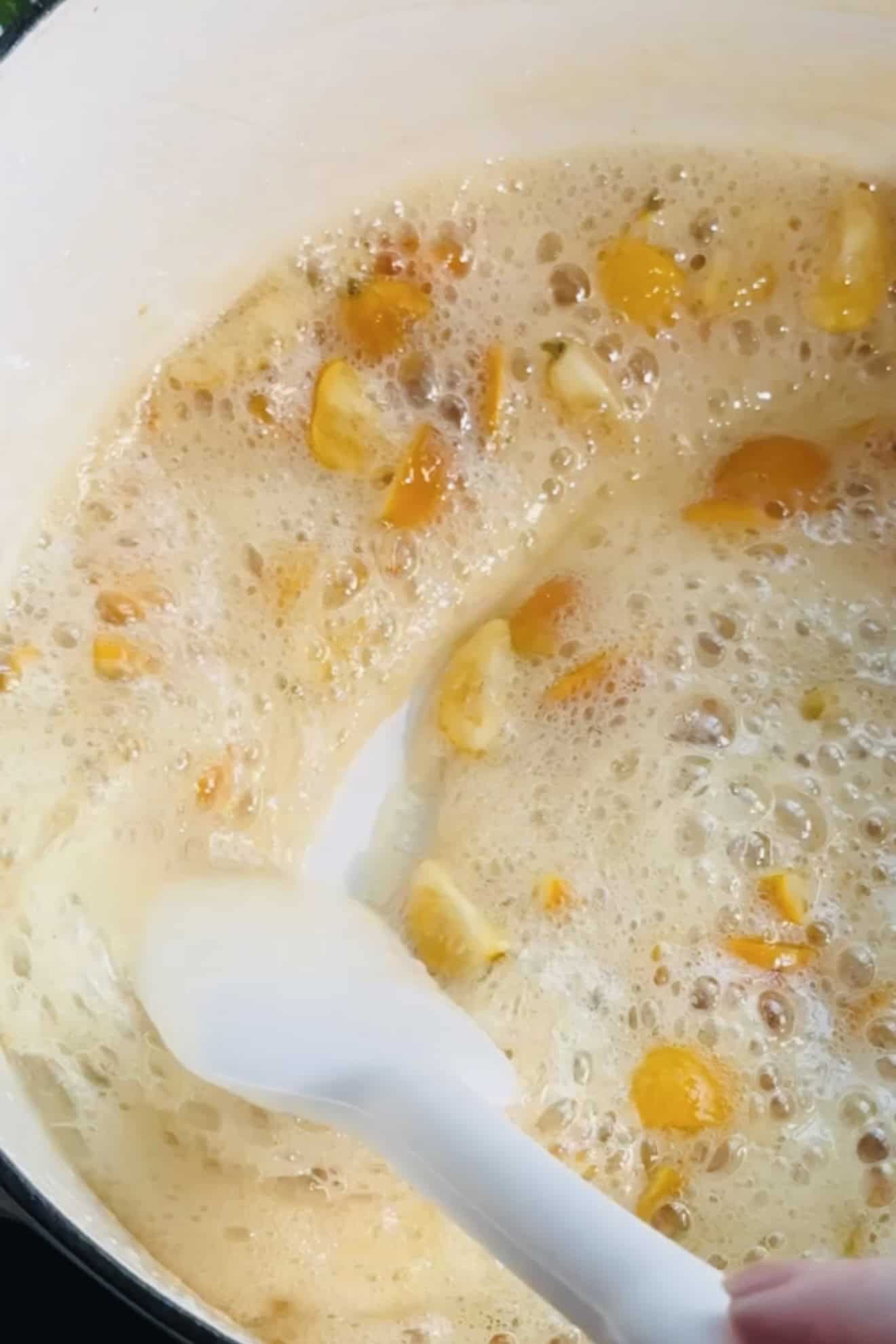 Kumquats in syrup bubbling and being candied in a pot. 