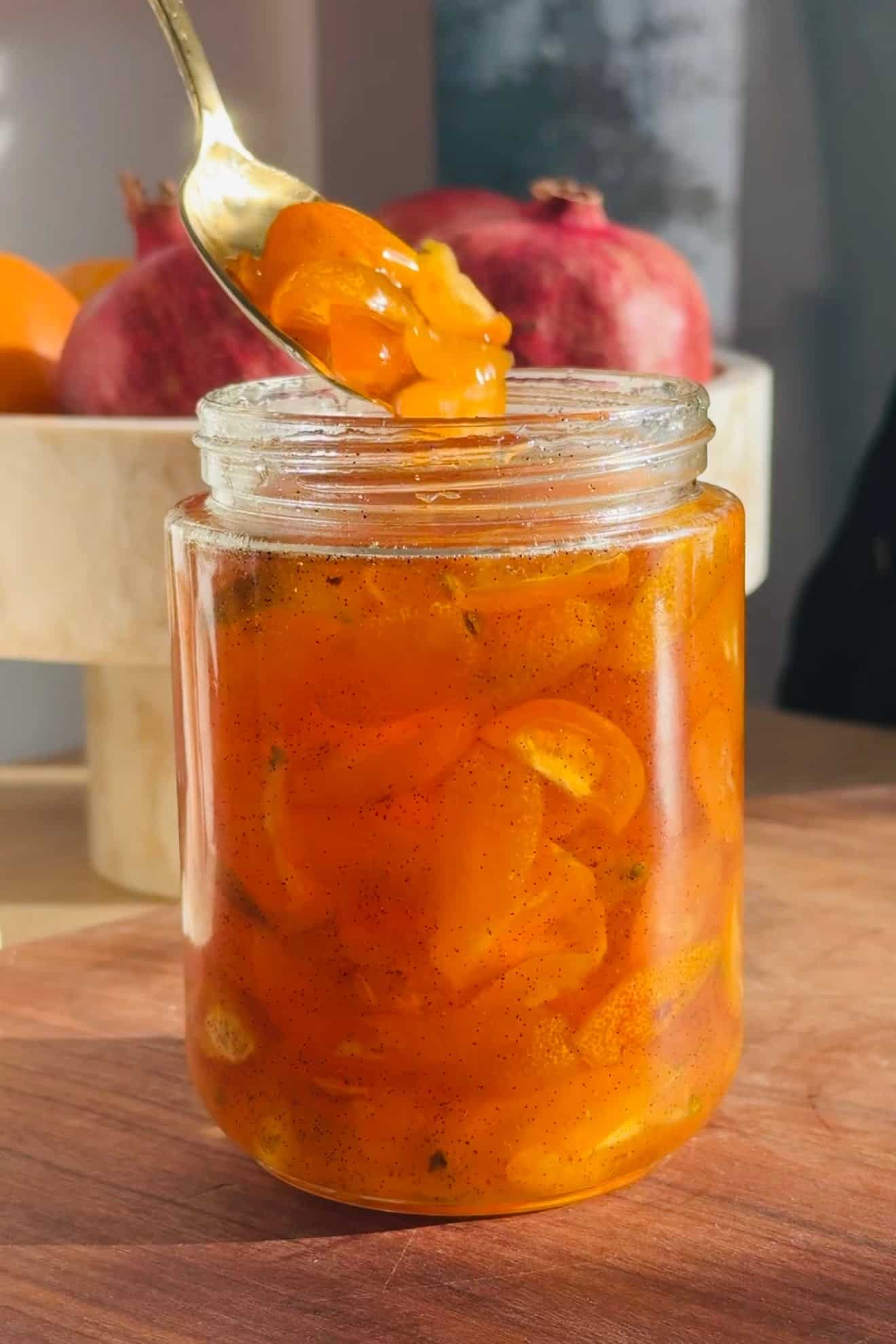 Candied kumquats in a glass jar with a spoon.